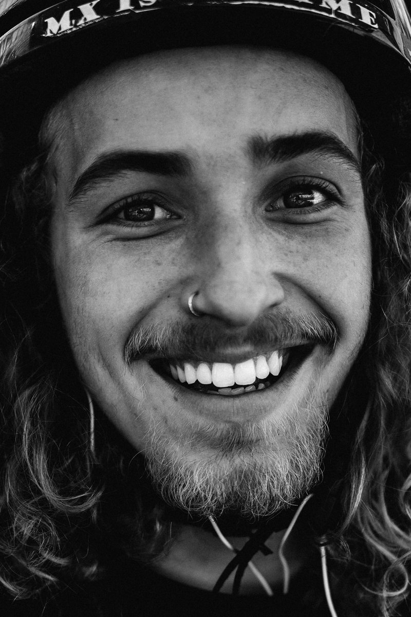 Close-up smiling portrait of a young man wearing a helmet with curly hair and a nose ring. by Sydney SG