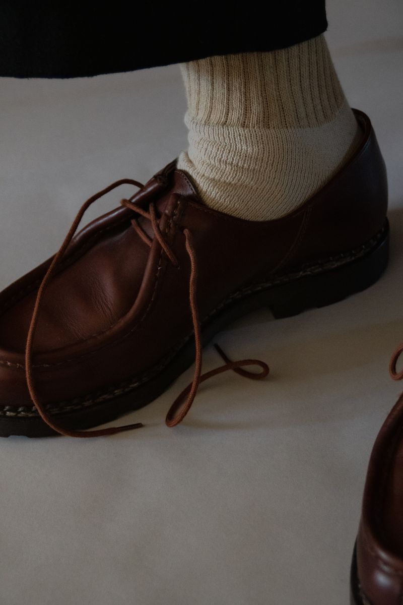 Detailed study of a red-brown, leather loafer with cream ribbed sock. The rich textures and precise composition transform everyday attire into a meditation on craftsmanship and care. by Sydney SG