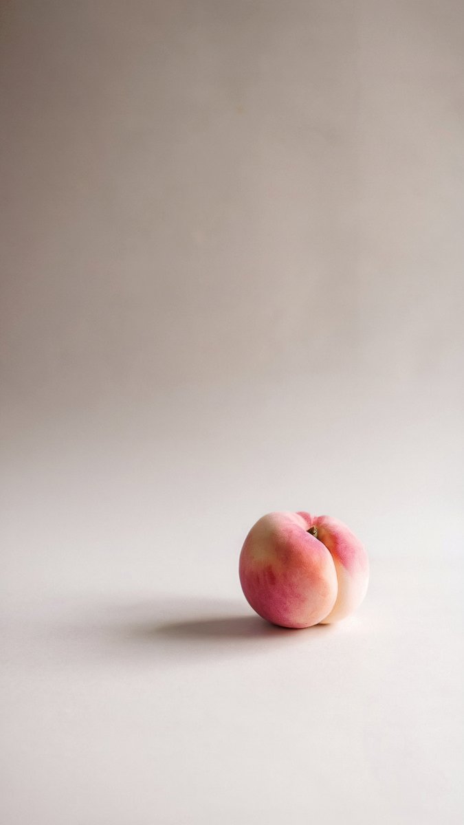 A single peach with pink and yellow hues, placed on a minimal beige background with soft shadows. Image generated with AI. by Sydney SG