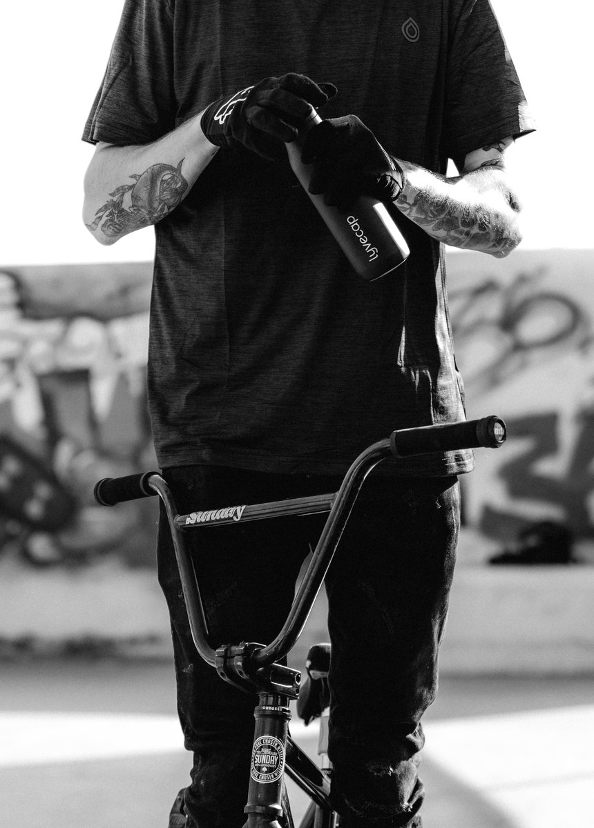 BMX rider holding a black matte water bottle while standing next to a bike in a skatepark. by Sydney SG