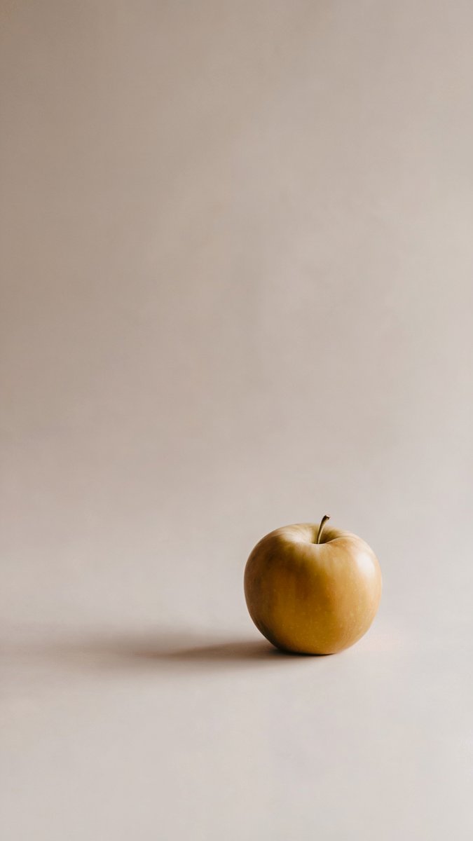 A single golden apple on a light beige background, softly lit from above with a subtle shadow. Image generated with AI. by Sydney SG