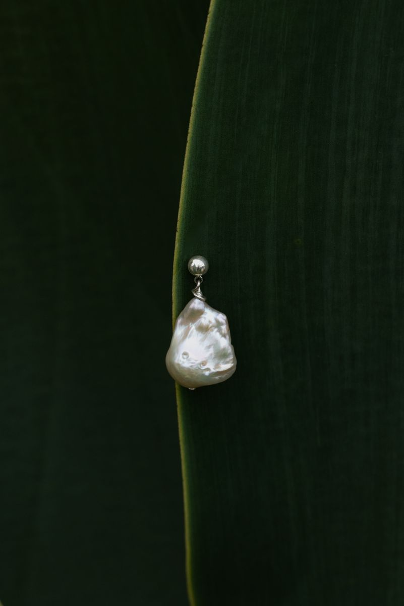 A single silver pearl earring displayed on a large agave leaf. The smooth organic curves of the leaf complement the natural form of the pearl. by Sydney SG