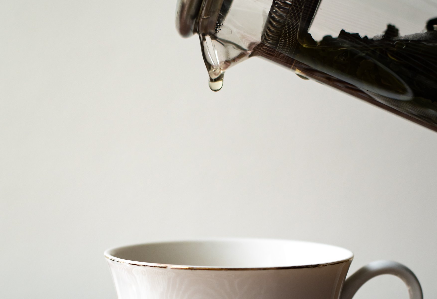 A clear glass teapot pouring a single droplet of liquid into a delicate white teacup. by Sydney SG