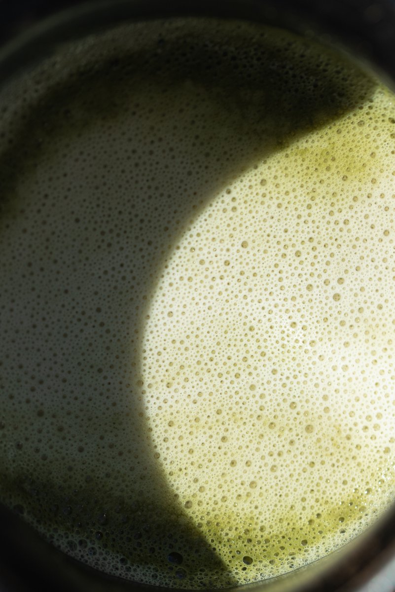 Overhead view of a matcha with bubbles forming on the surface, partially shadowed by the edges of the mug. by Sydney SG