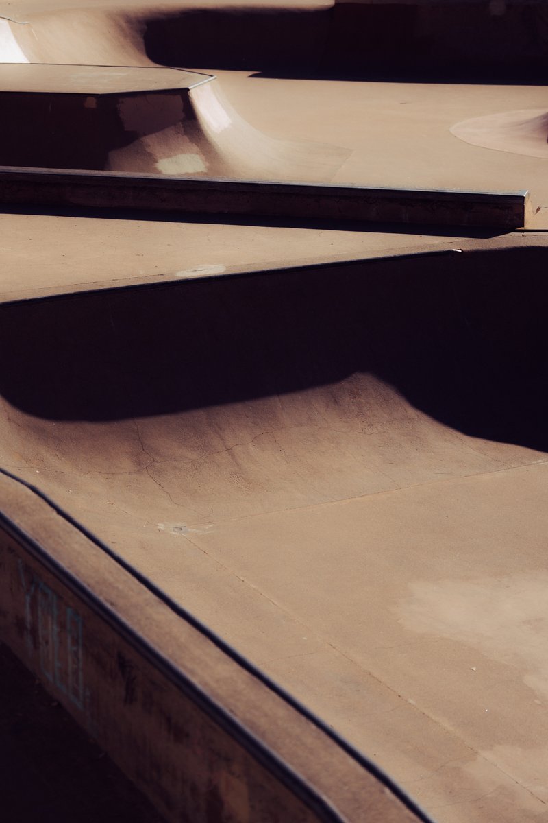 Abstract view of a skatepark with soft, flowing concrete ramps and deep shadows cast by the curves. by Sydney SG