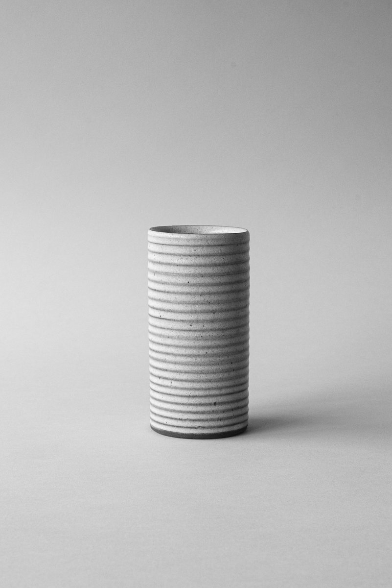 Tall, cylindrical stoneware vase with horizontal ridges, placed against a minimalist neutral background. by Sydney SG