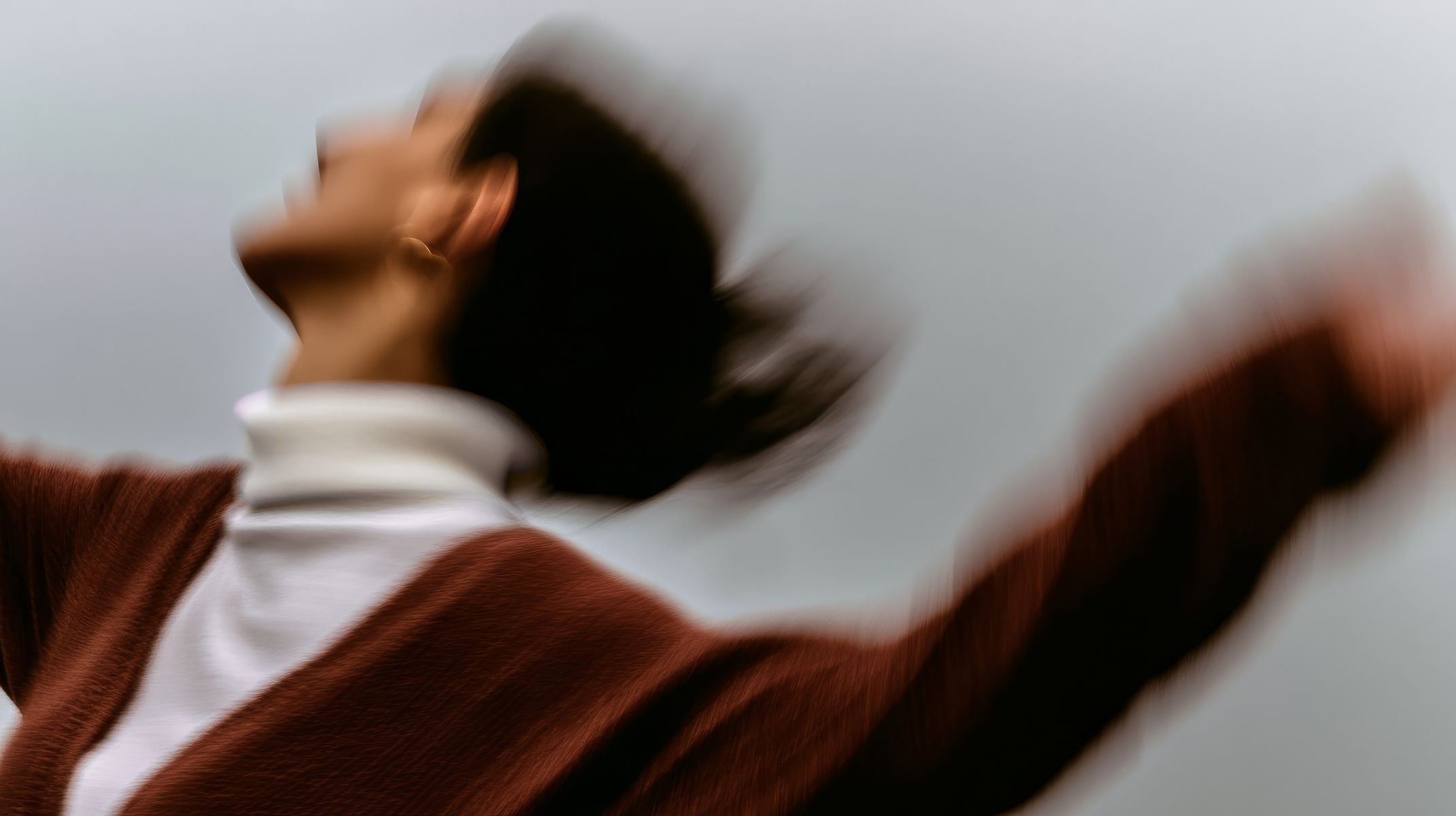 A person in rust-colored clothing photographed with intentional motion blur against an overcast sky. The movement creates flowing, streaked forms throughout the frame. (AI-generated image) by Sydney SG