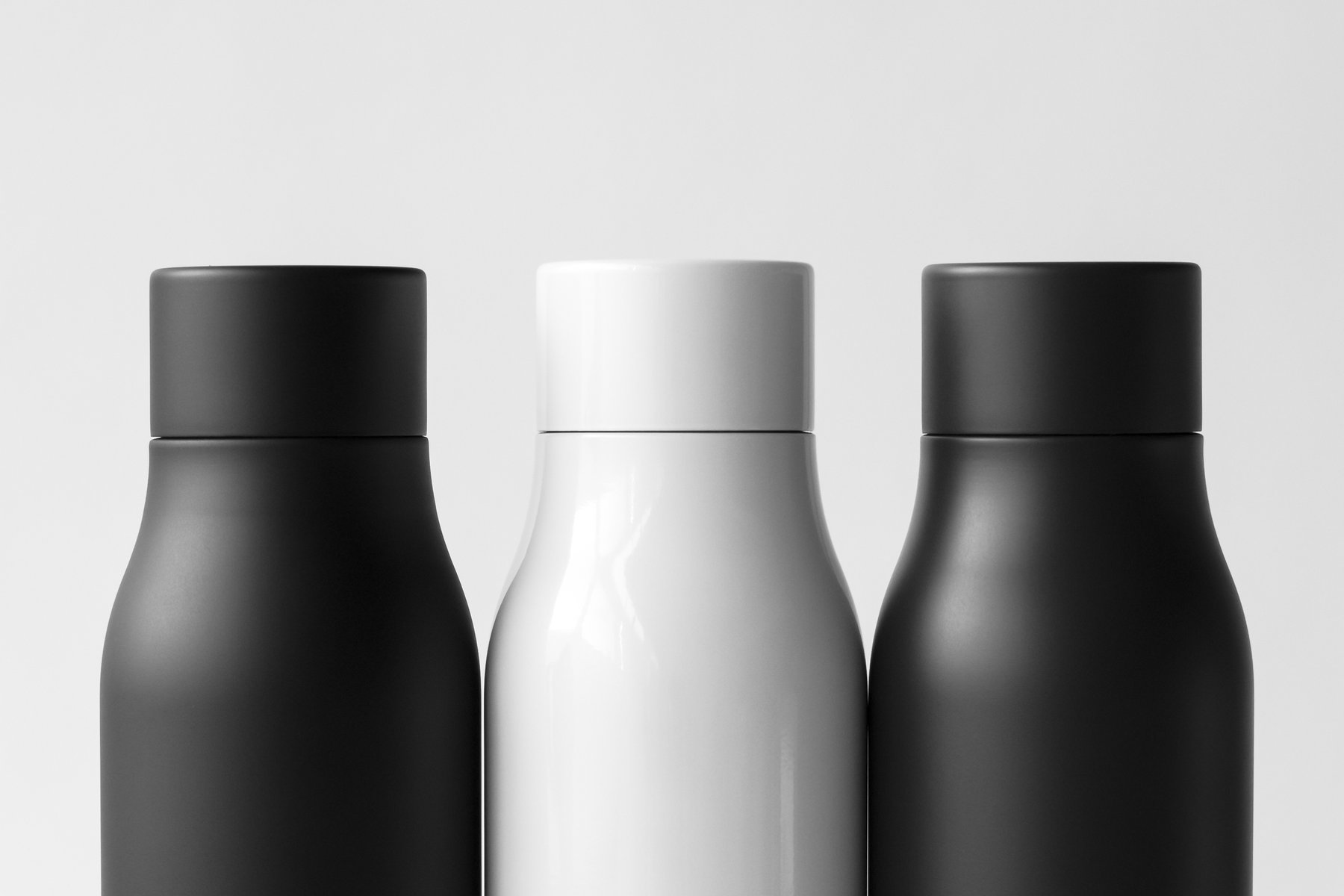 Three water bottles, charcoal, black, and shimmery white, standing in a row against a light gray background. by Sydney SG