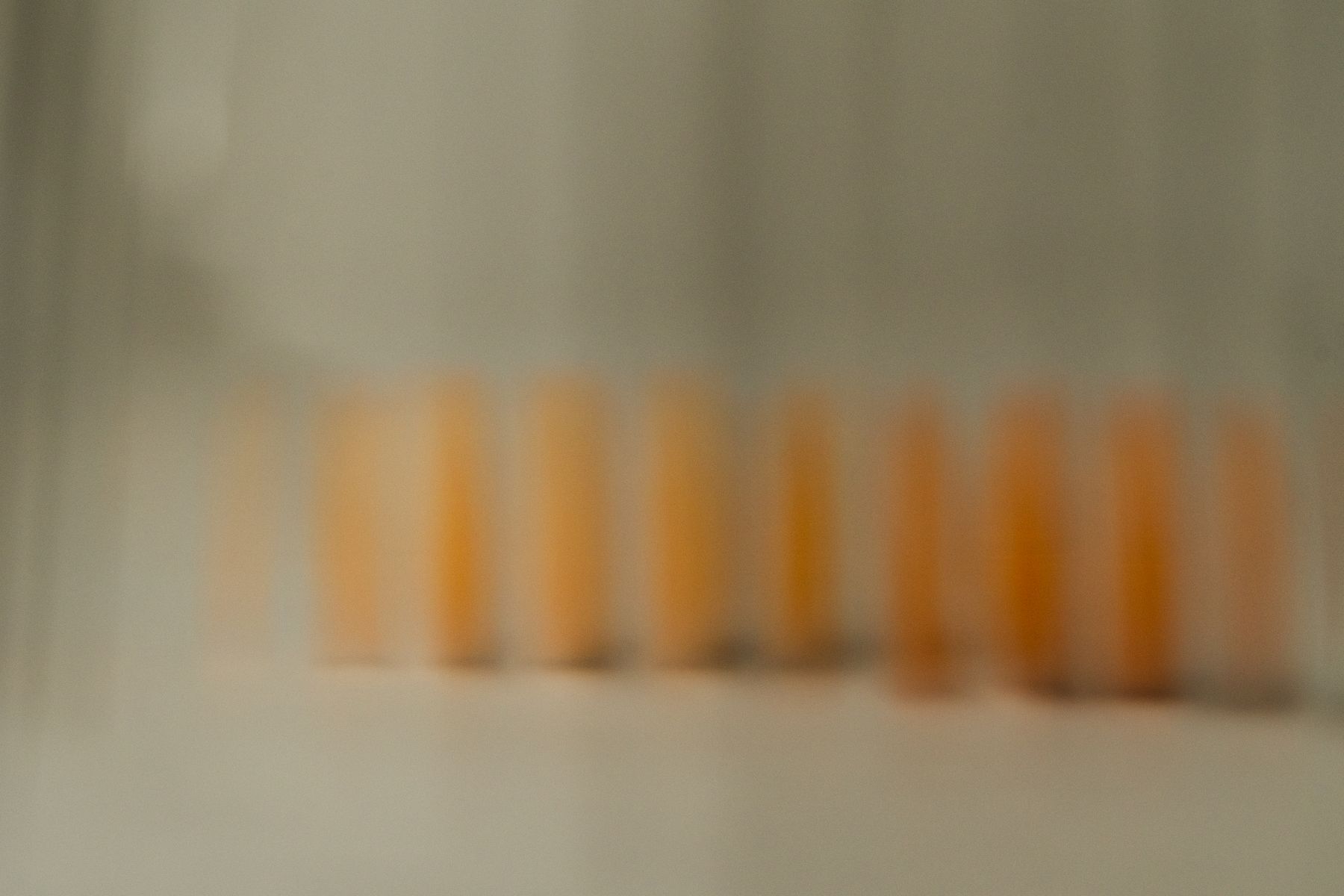 Extremely soft-focus image of orange-yellow forms reflected in a row against a neutral background. The deliberate blur transforms the objects into an abstract rhythm of warm color. by Sydney SG