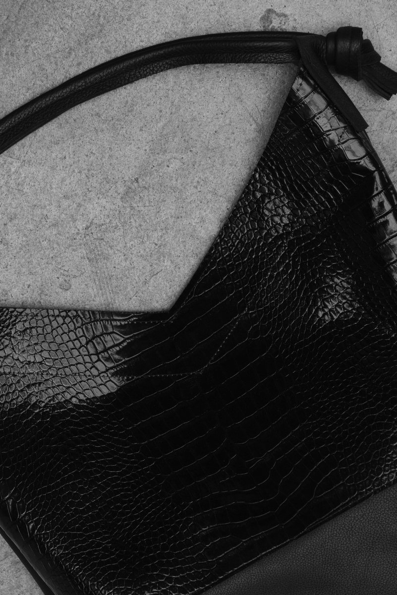 Close-up of a textured black leather handbag with a crocodile pattern, lying flat on a concrete surface. by Sydney SG