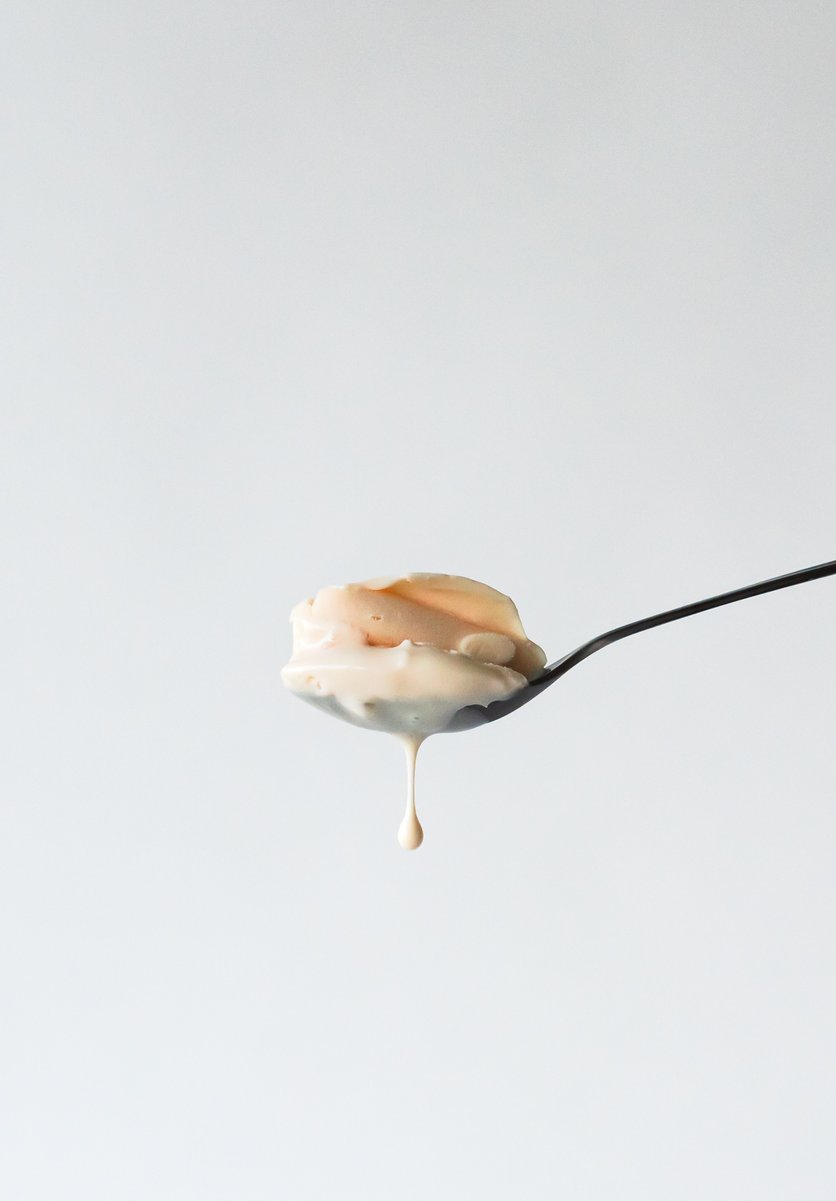 Side view of a spoonful of negroni gelato, a droplet hanging from the bottom edge, set against a plain white backdrop. by Sydney SG