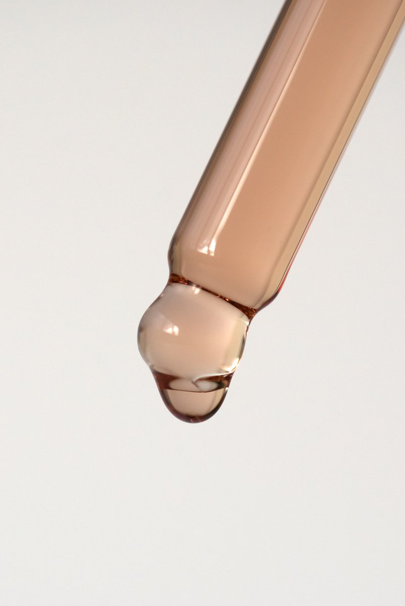 Close-up of a glass dropper releasing a single clear drop, set against a light, blurred background. by Sydney SG