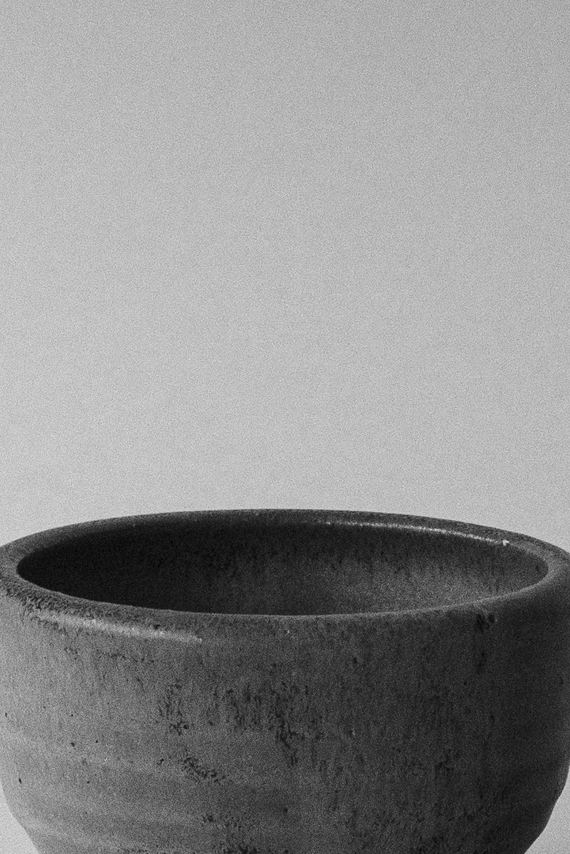 The top portion of a rough, dark ceramic cup in a minimalist composition. by Sydney SG