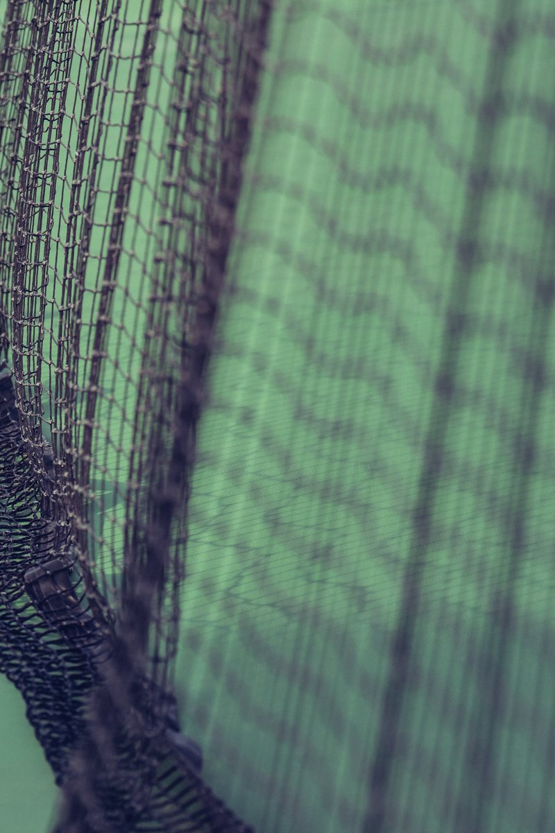 Close-up of a tennis net with green and black cords, creating a geometric pattern. by Sydney SG