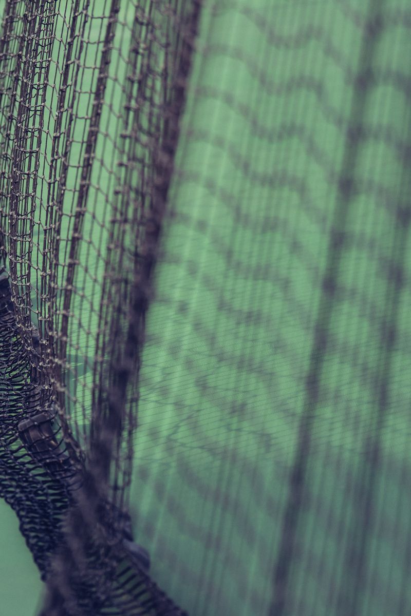 Close-up of a tennis net with green and black cords, creating a geometric pattern. by Sydney SG