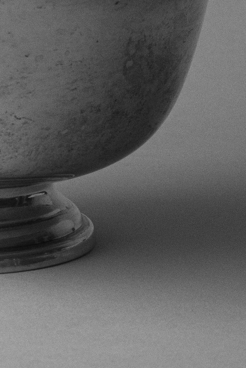 Partial view of a sterling silver bowl base with a worn, textured surface, captured in shadow against a neutral background. by Sydney SG