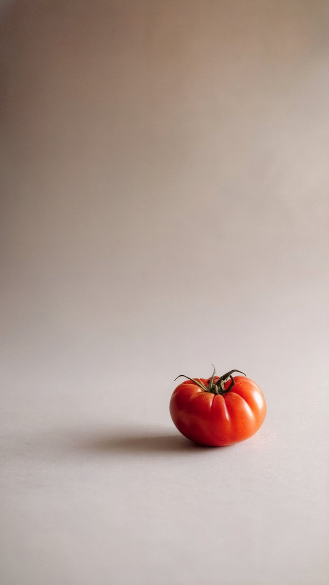 A vibrant red tomato resting on a beige background with soft, natural lighting and a faint shadow. Image generated with AI. by Sydney SG