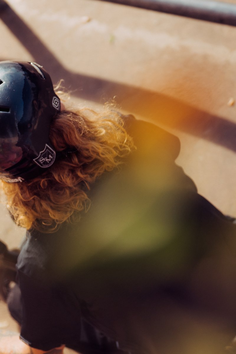 Overhead shot of a person wearing a black helmet with curly hair, partially obscured by yellow leaves. by Sydney SG