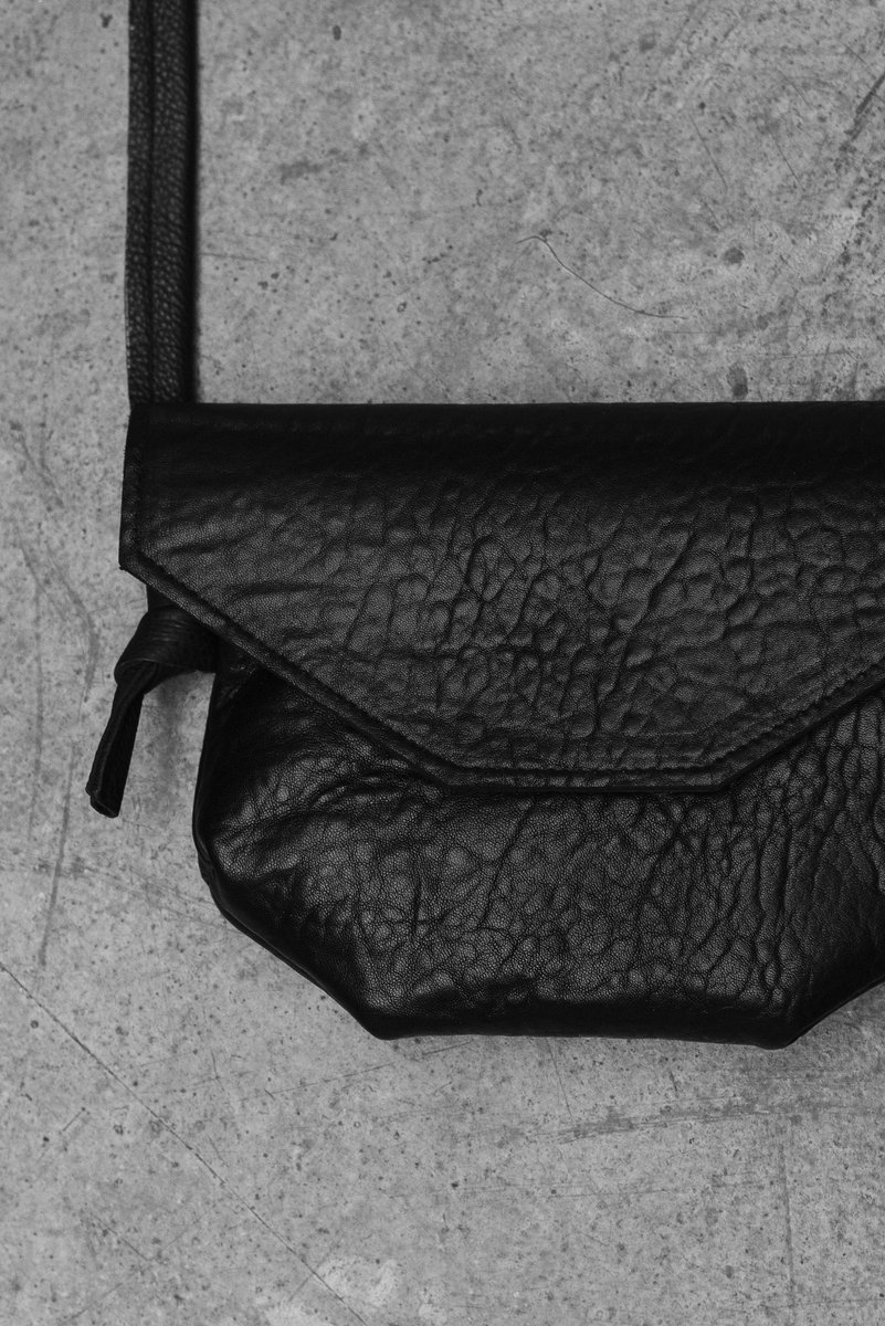 Close-up of a black leather purse with a pebbled texture, set on a rough concrete background. by Sydney SG