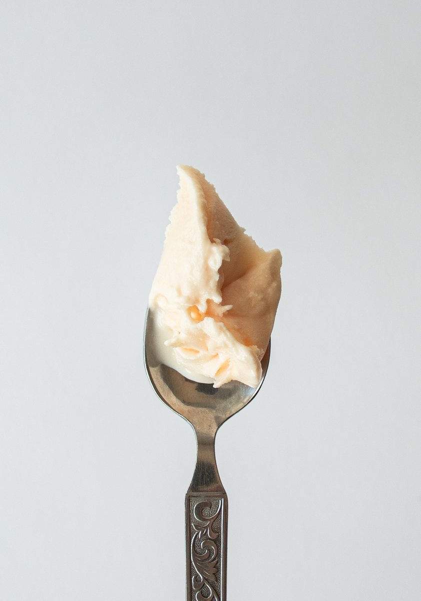 Close-up of a dollop of negroni-flavored gelato on a decorative silver spoon against a light background. by Sydney SG