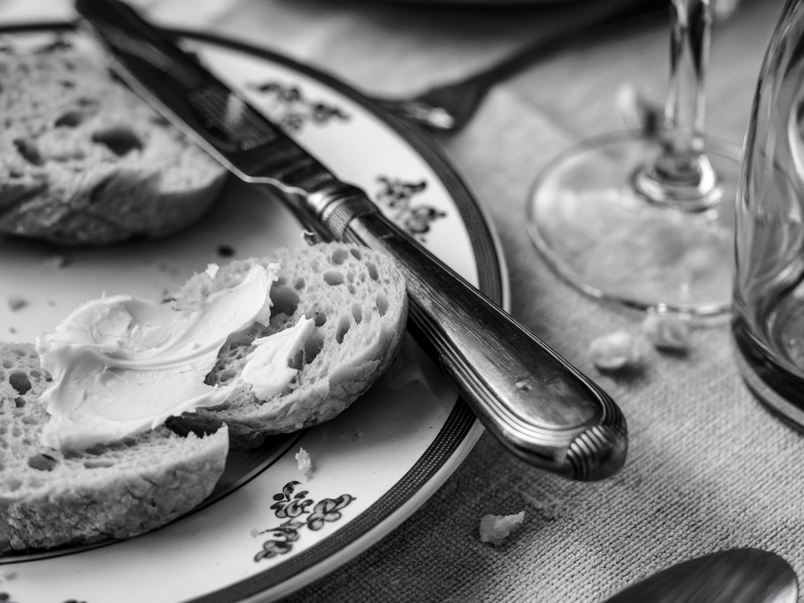 Monochromatic close-up of bread and butter on a vintage plate, with a butter knife resting on the side. A rustic, elegant table setting captured in soft lighting. Image generated with AI. by Sydney SG