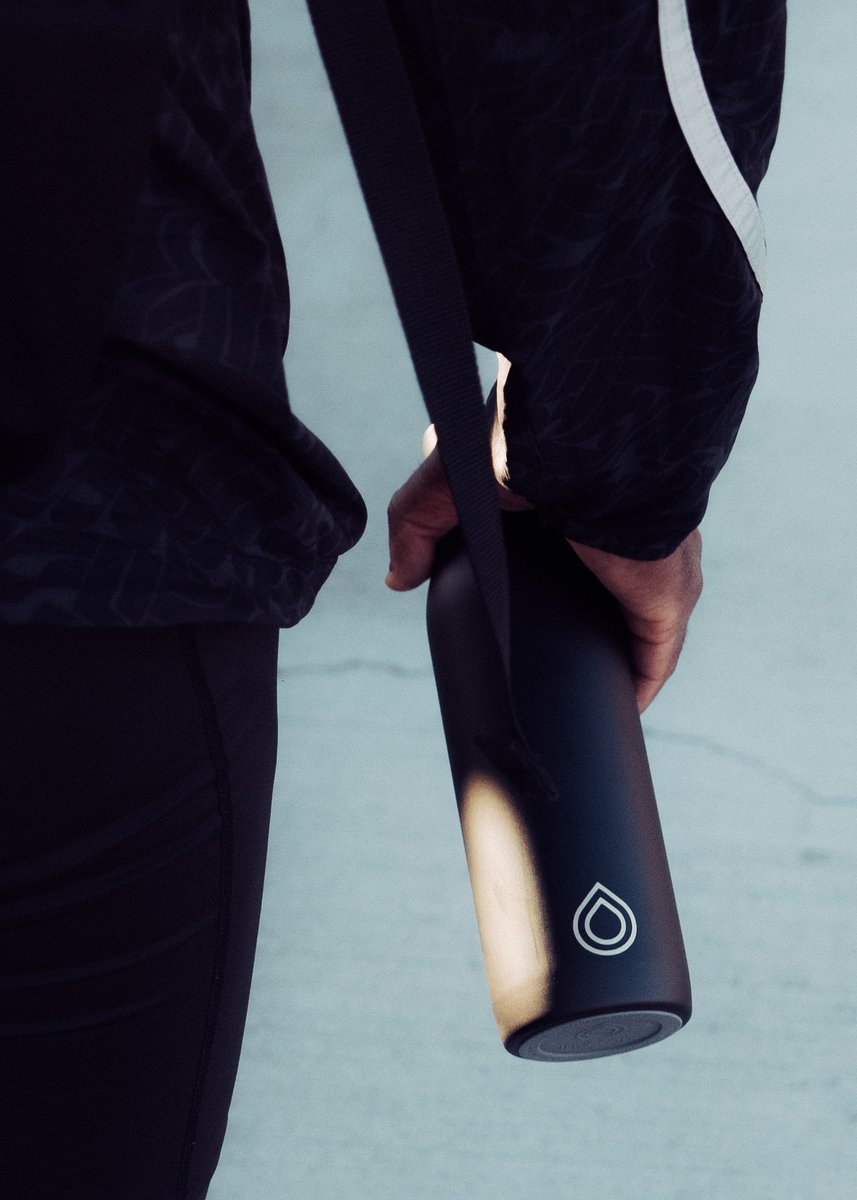 Person holding a black matte water bottle with a minimalist logo while walking outdoors in athletic wear. by Sydney SG